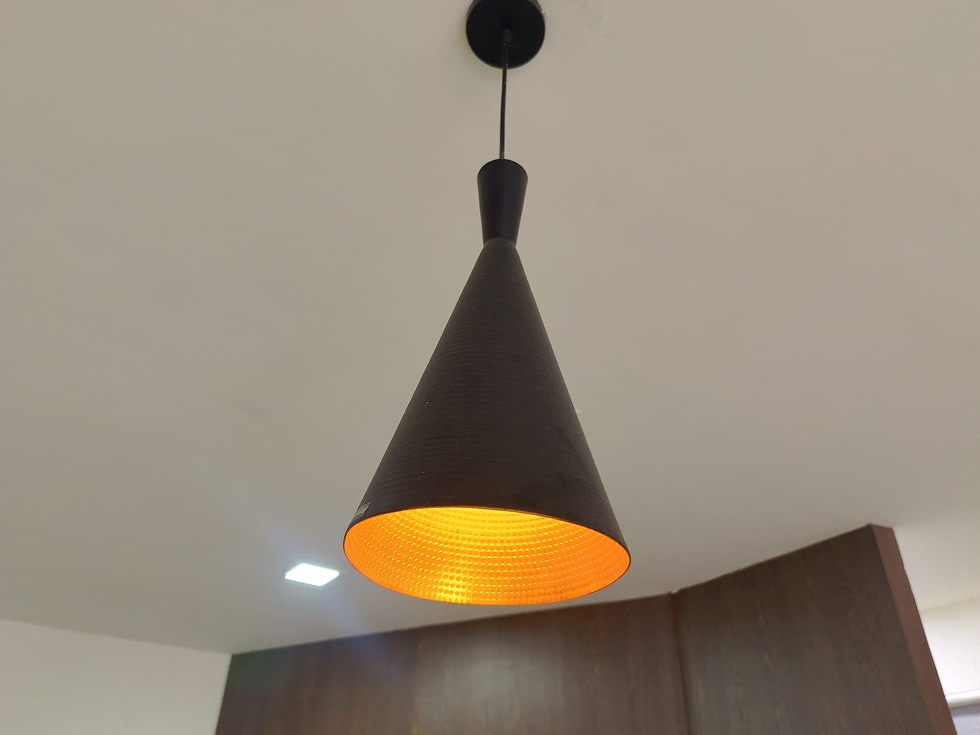 Modern black pendant light with warm glow hanging from a ceiling