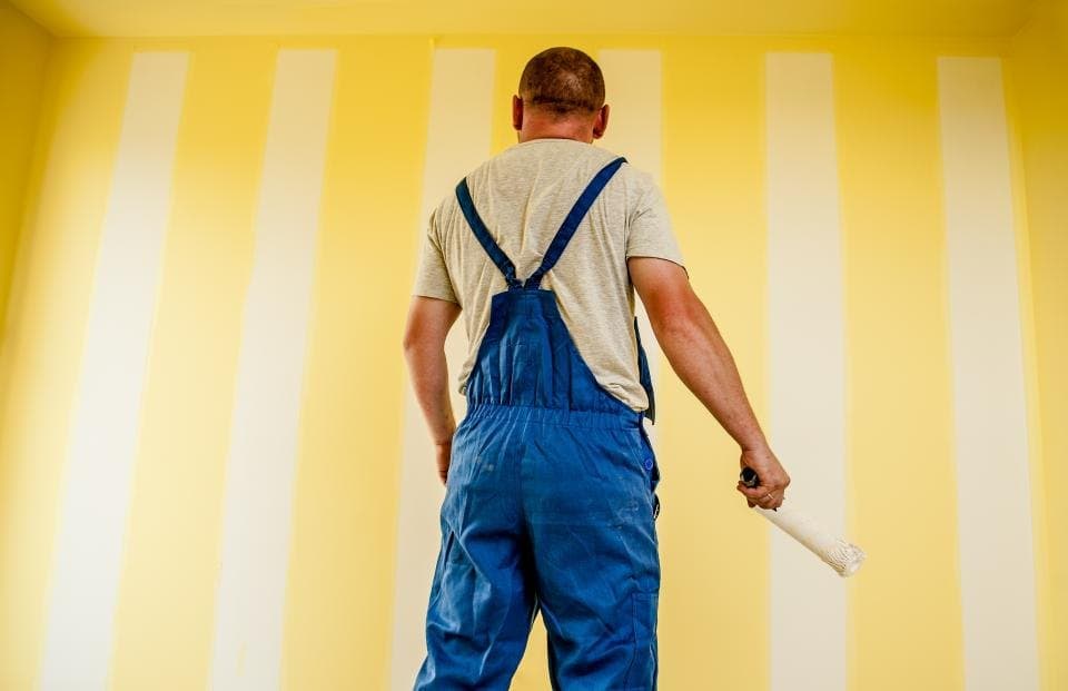 Painter in overalls painting an interior wall with a roller